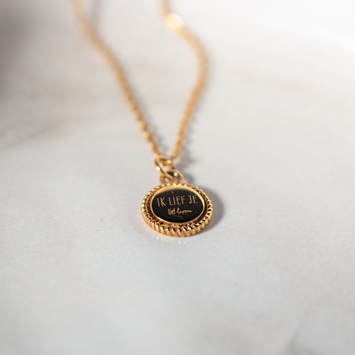 Gouden Lief Leven ketting met hanger en de tekst 'Ik lief je' op een zachte marmeren achtergrond.