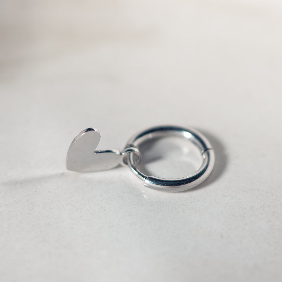 Zilveren Lief Leven oorbel met hartvormige bedel op een zachte marmeren achtergrond.