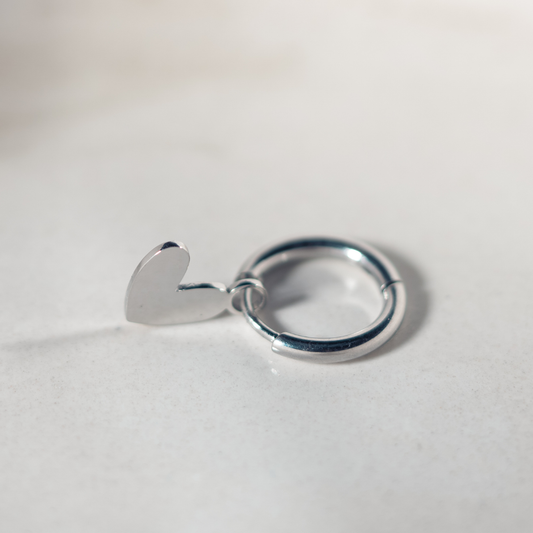 Zilveren Lief Leven oorbel met hartvormige bedel op een zachte marmeren achtergrond.